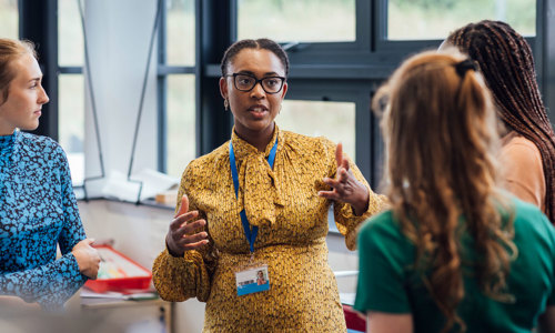 a woman in a yellow dress talking to a woman in a classroom
